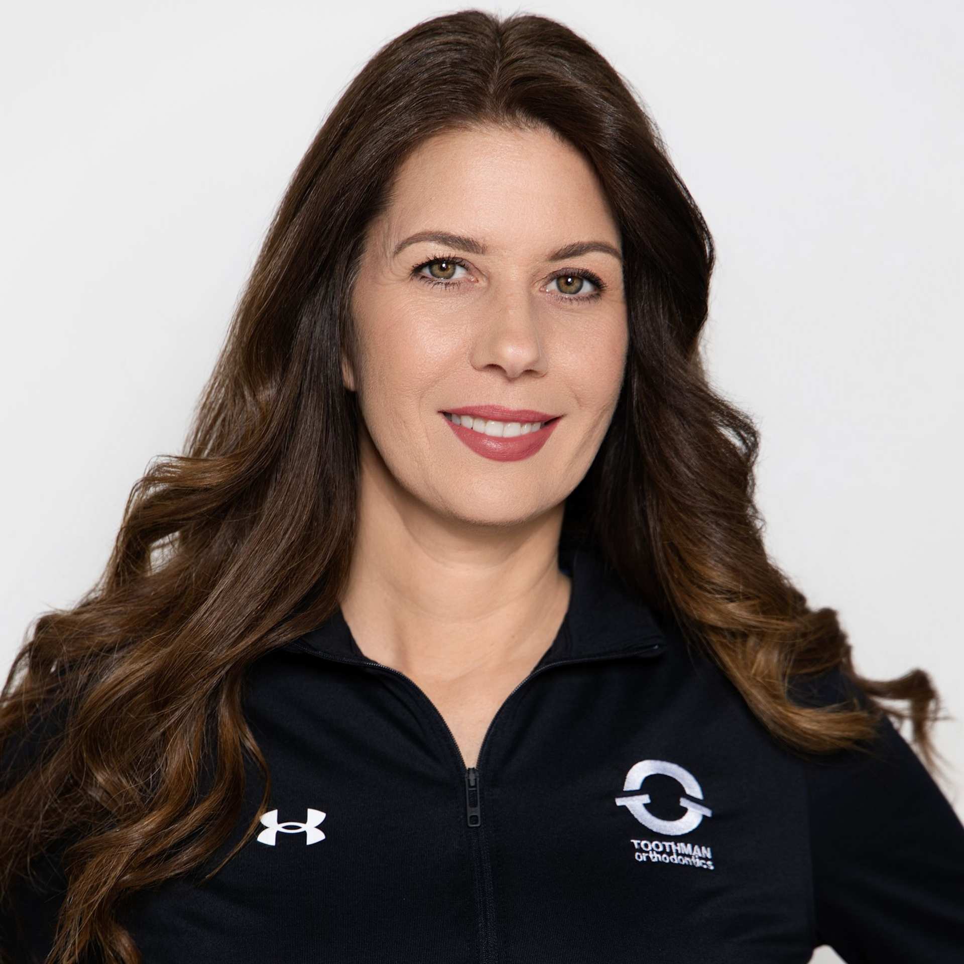 Woman with long brown hair wearing a black zip-up athletic jacket and smiling against a white background