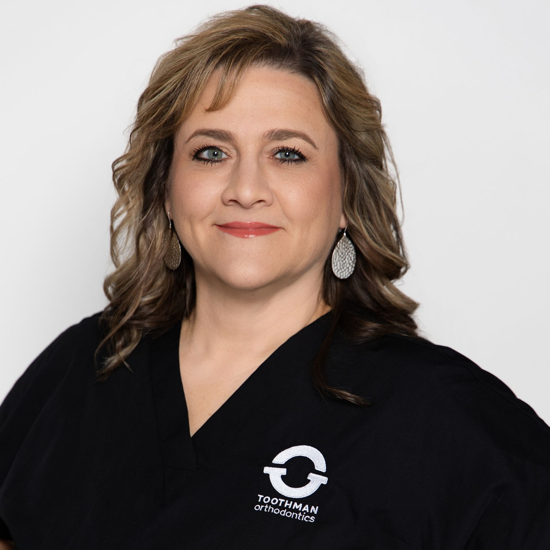 Woman in a black polo shirt with a company logo, standing against a plain light background.