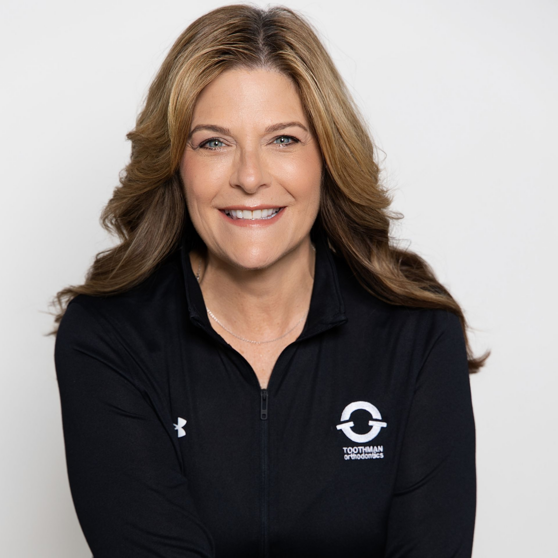 Smiling woman in a black zip-up jacket with a logo on a light gray background
