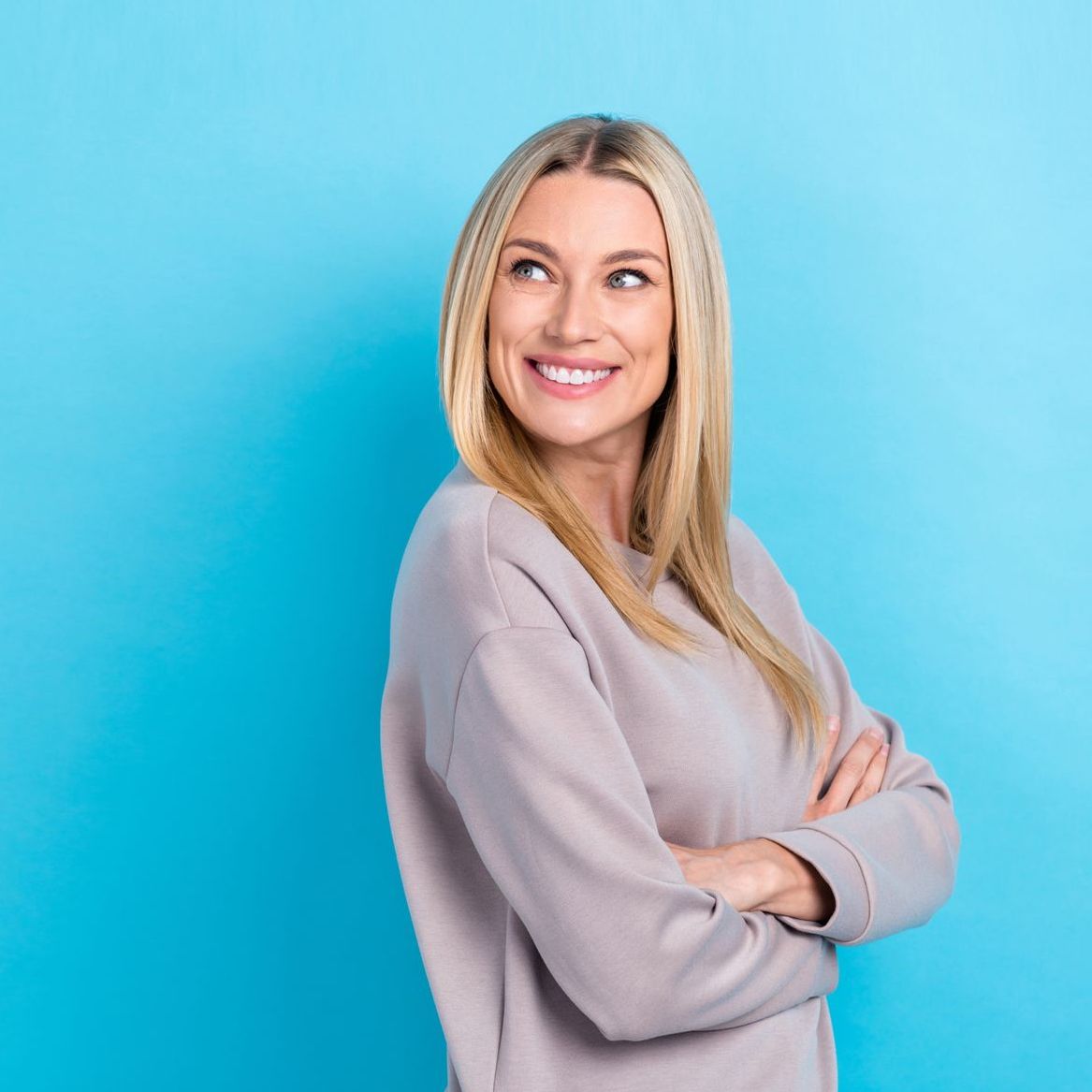 A woman is standing with her arms crossed and smiling.