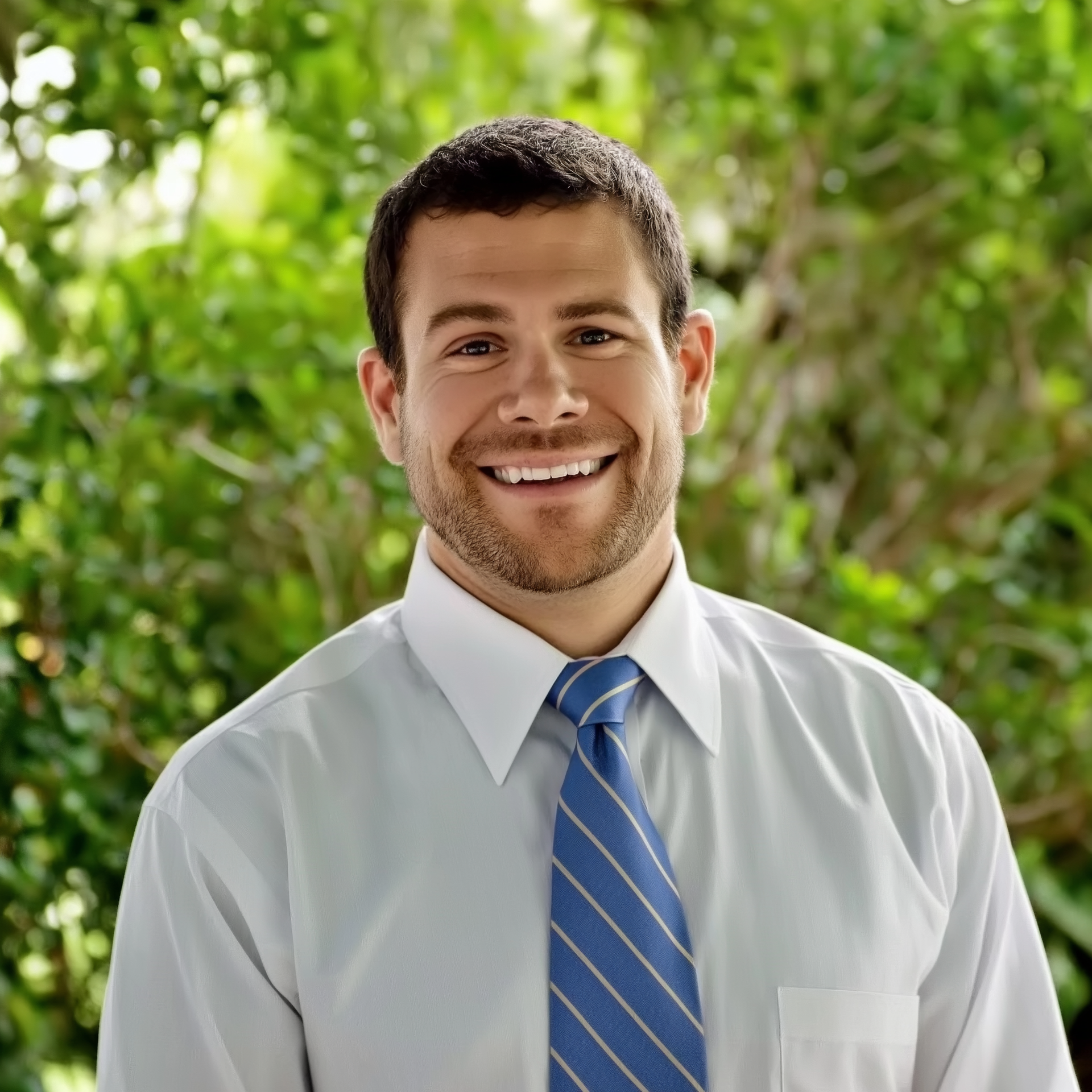 A man in a white shirt and blue tie smiles for the camera