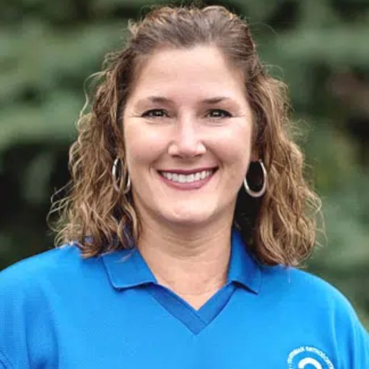 A woman wearing a blue shirt and hoop earrings is smiling for the camera.