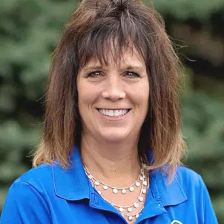 A woman wearing a blue shirt and a necklace is smiling for the camera.