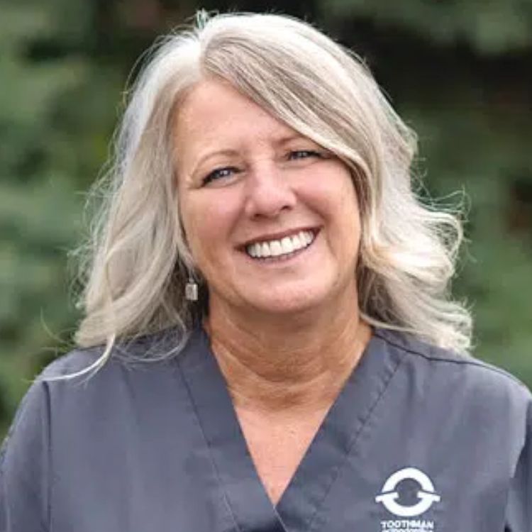 A woman wearing a scrub top is smiling for the camera.
