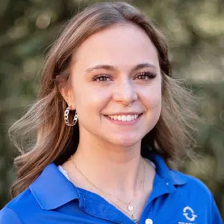 A woman wearing a blue shirt and hoop earrings is smiling for the camera.