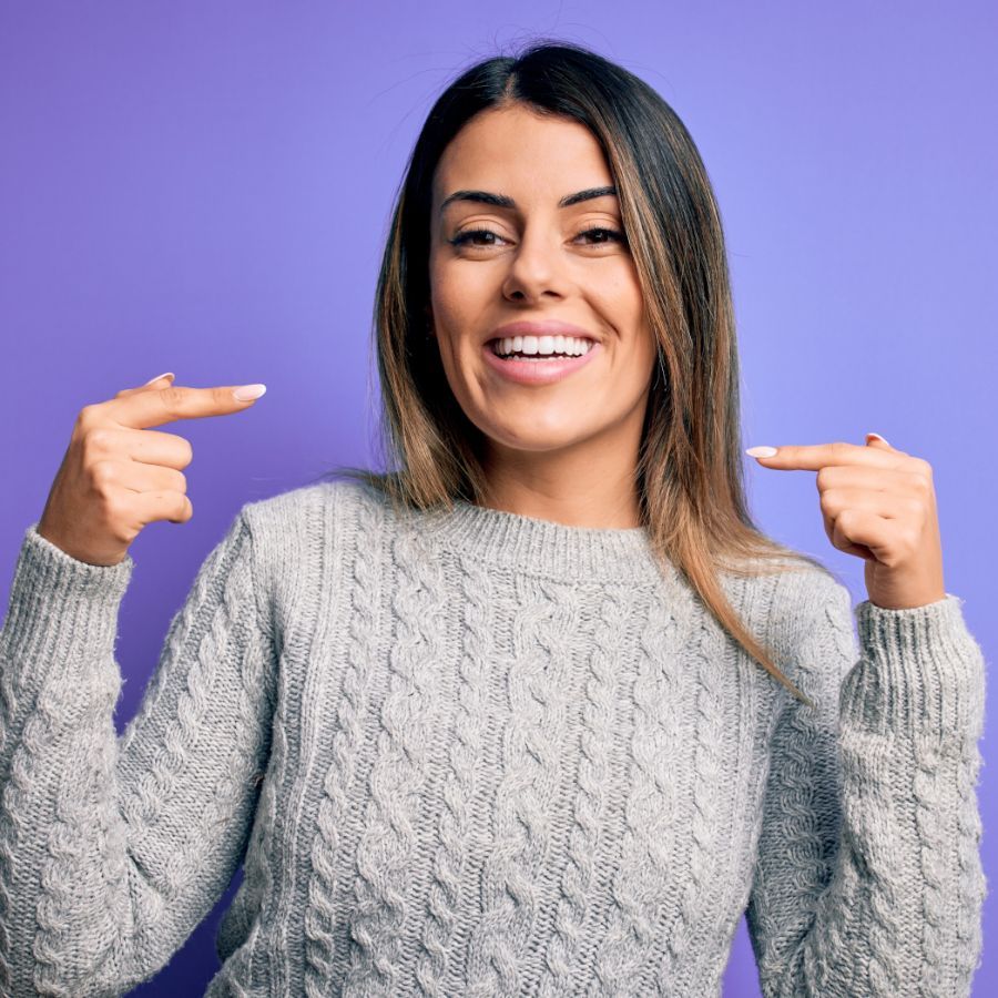 A woman in a sweater is pointing at herself.