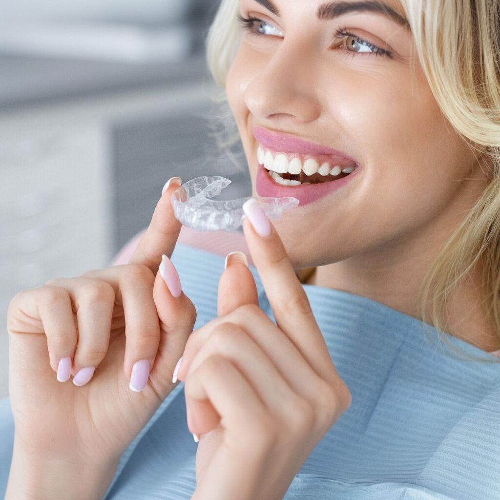 Woman smiling, holding clear dental aligners near her teeth.