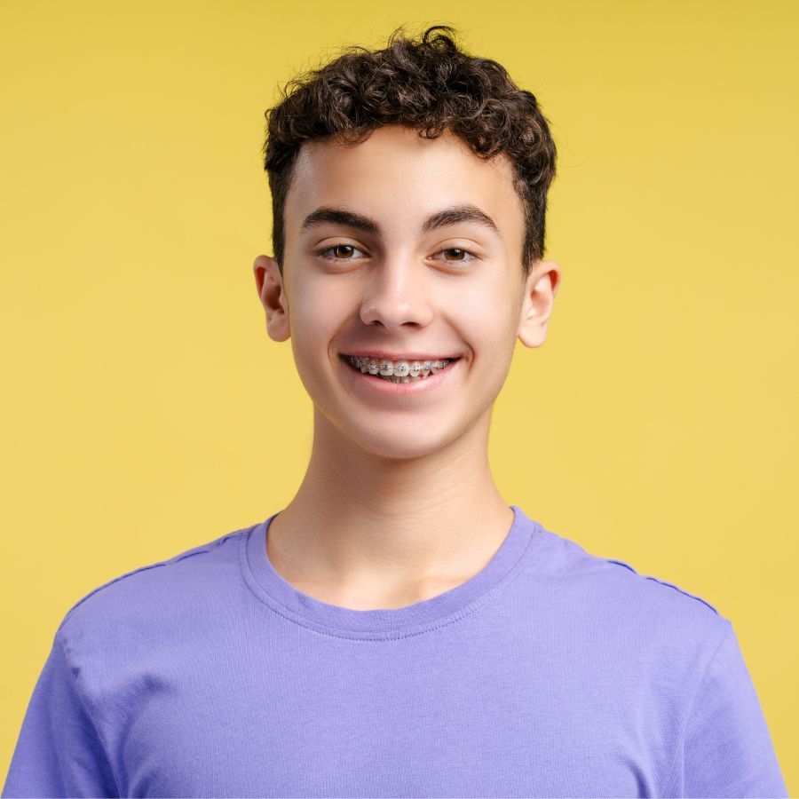 A young man with braces on his teeth is wearing a purple shirt and smiling.
