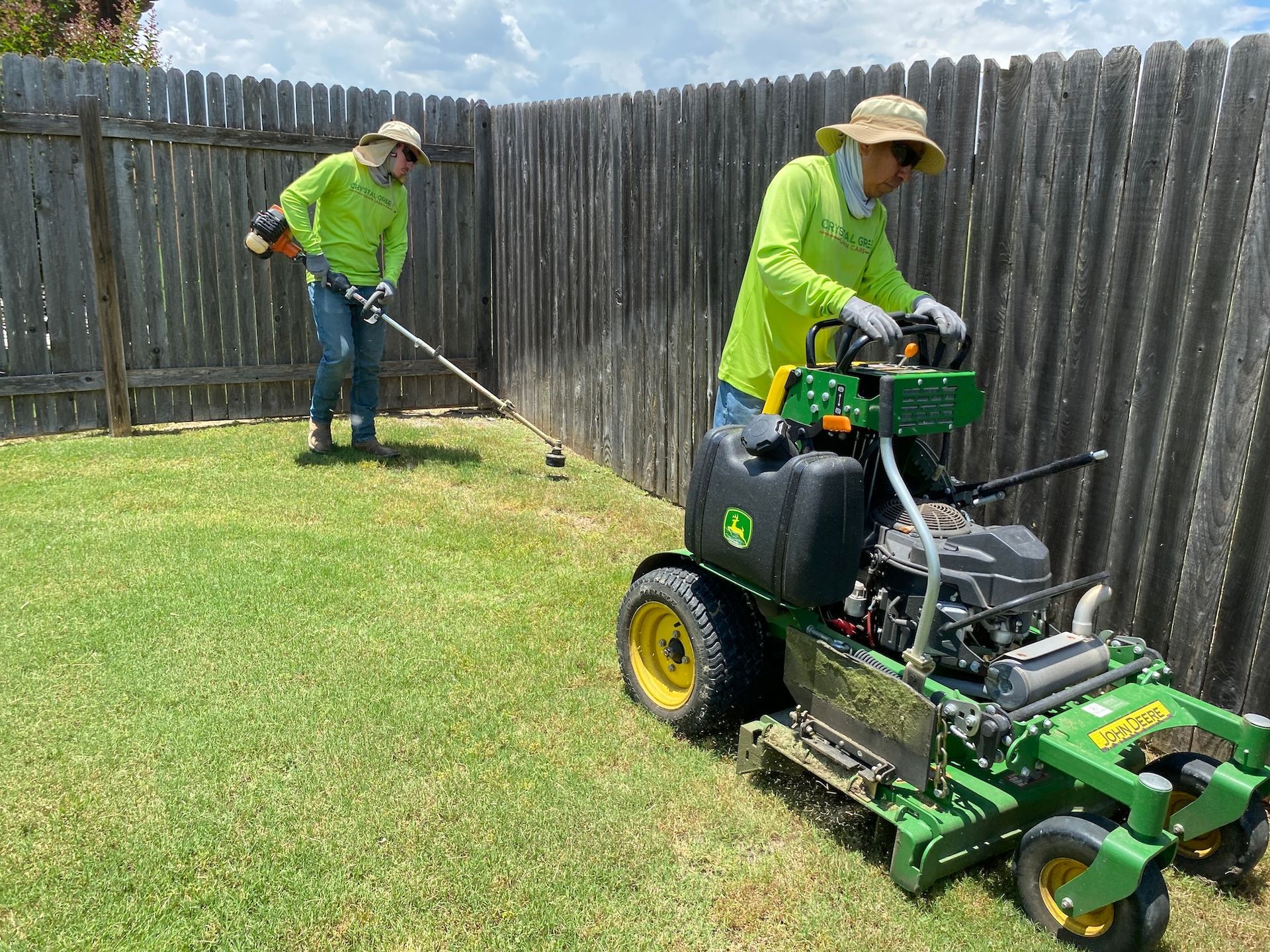a man is riding a lawn mower while another man is trimming the grass .