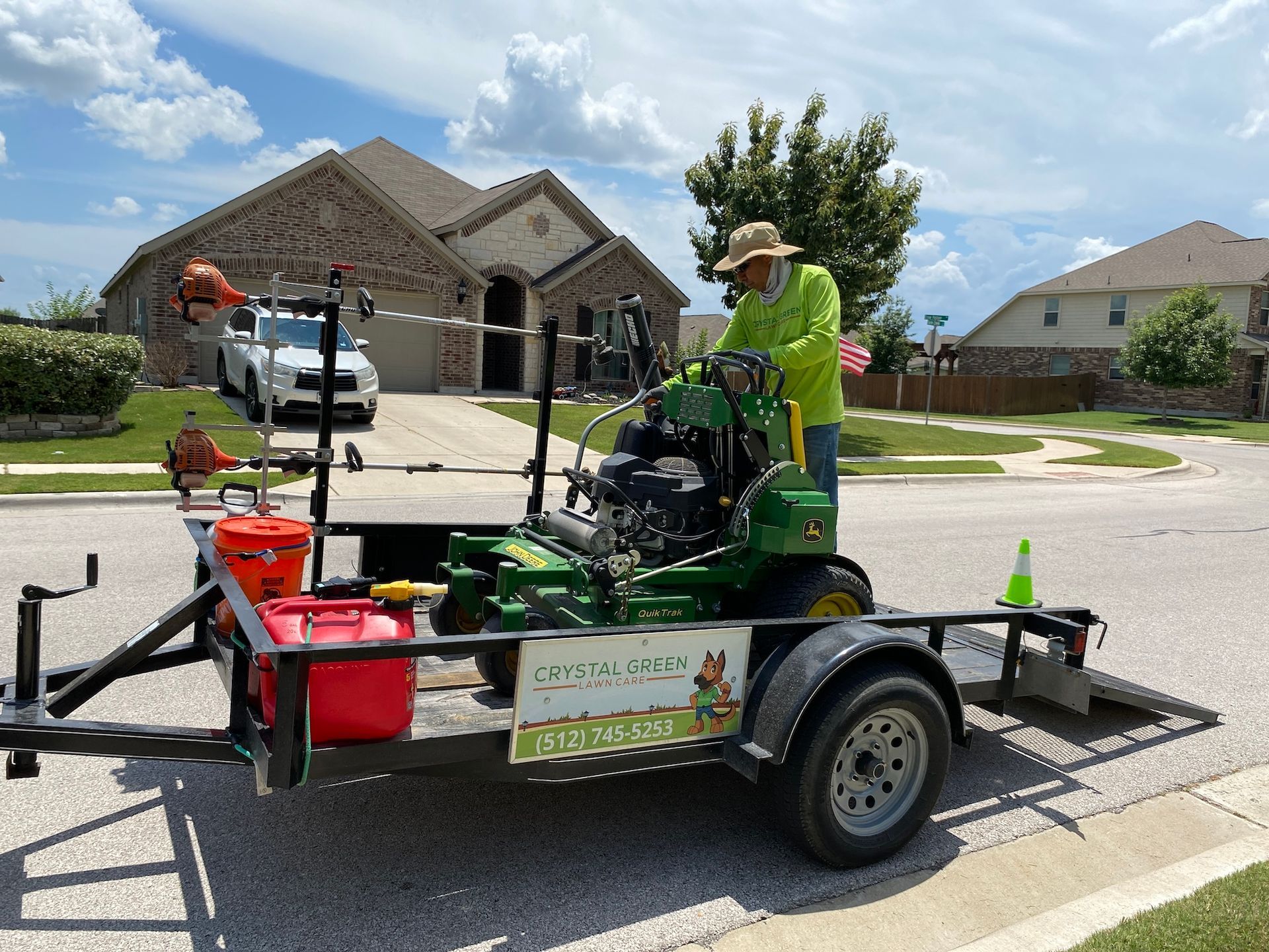 a man is driving a lawn mower on a trailer in front of a house .