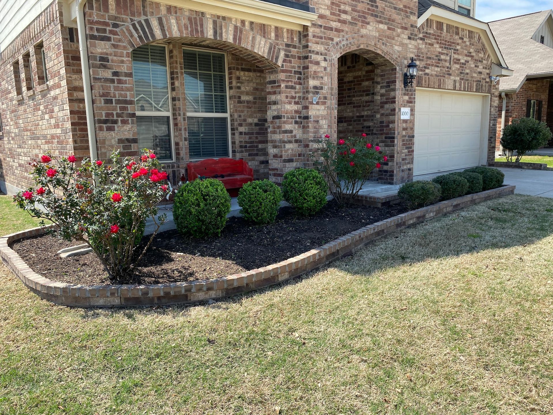 A brick house with a lush green lawn and flowers in front of it.
