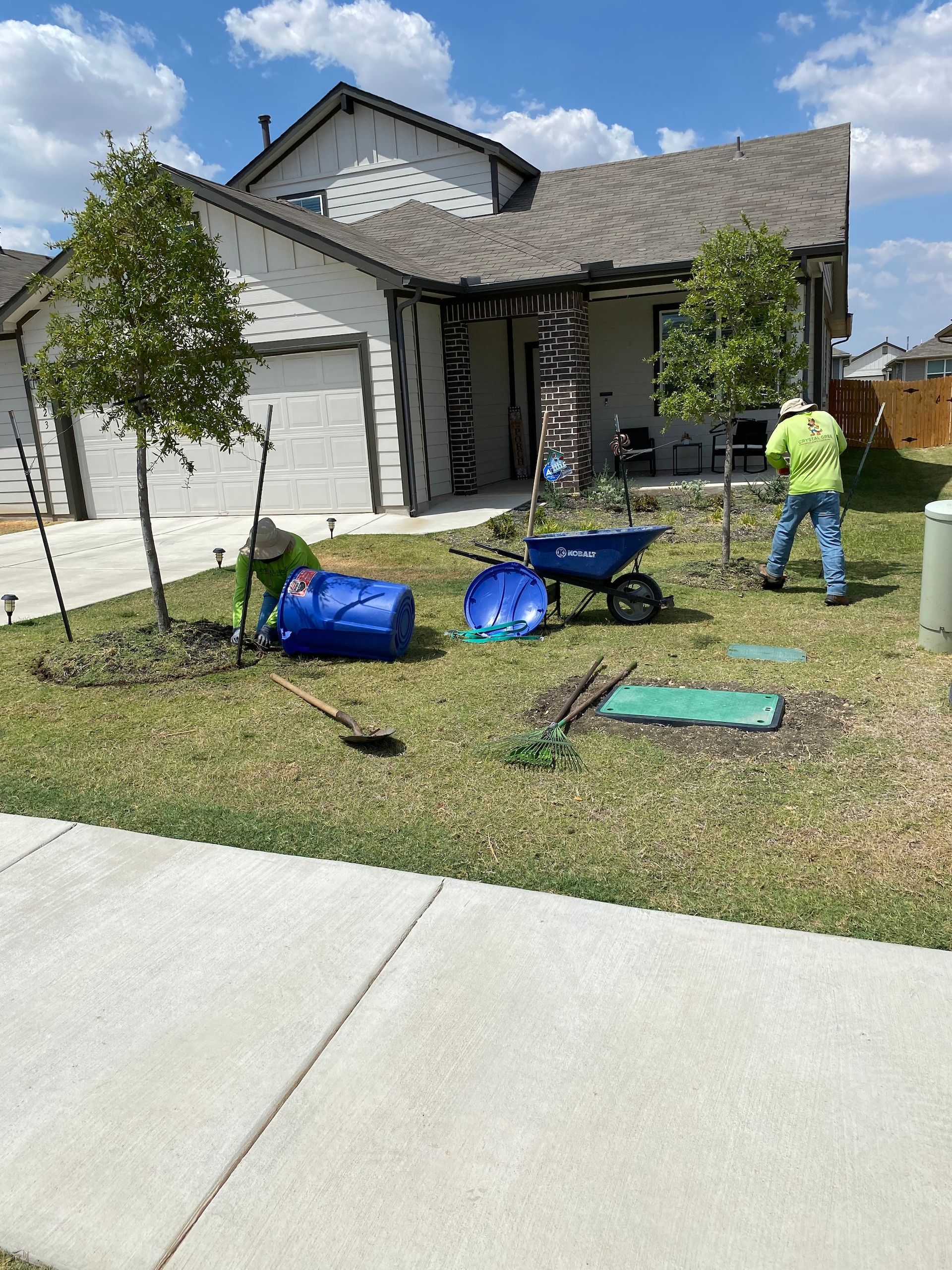 a man is standing in front of a house with a blue barrel and a wheelbarrow .