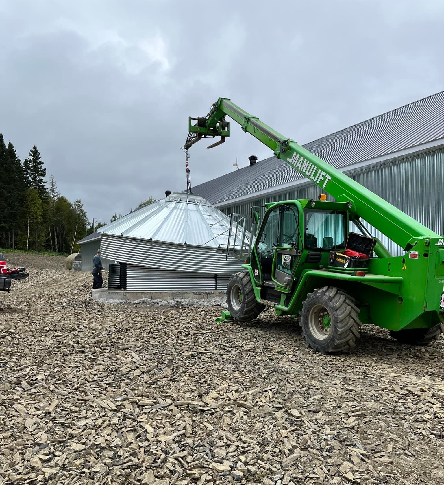 Un chariot élévateur vert travaille sur un silo devant un bâtiment.