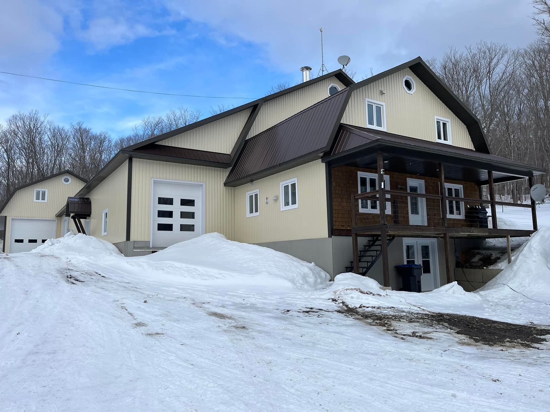 Une grande maison blanche avec un toit brun est entourée de neige.