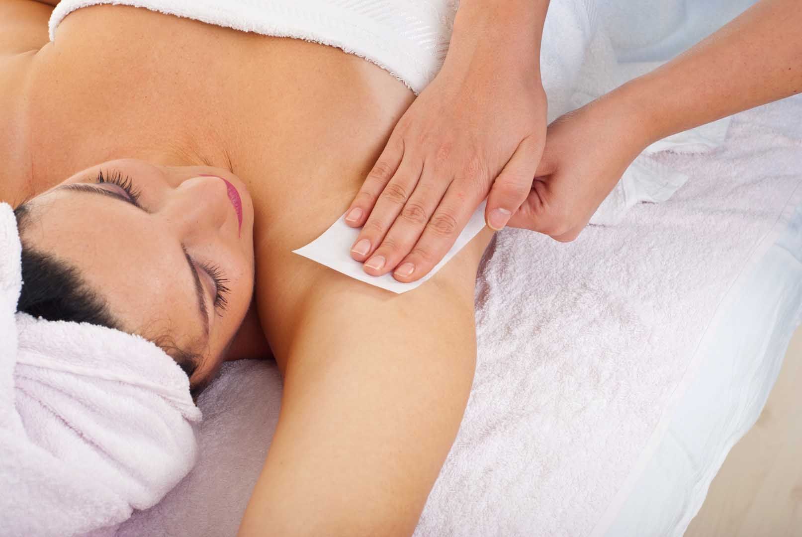 Woman having her underarm waxed at a spa; hands holding a strip, applying pressure.
