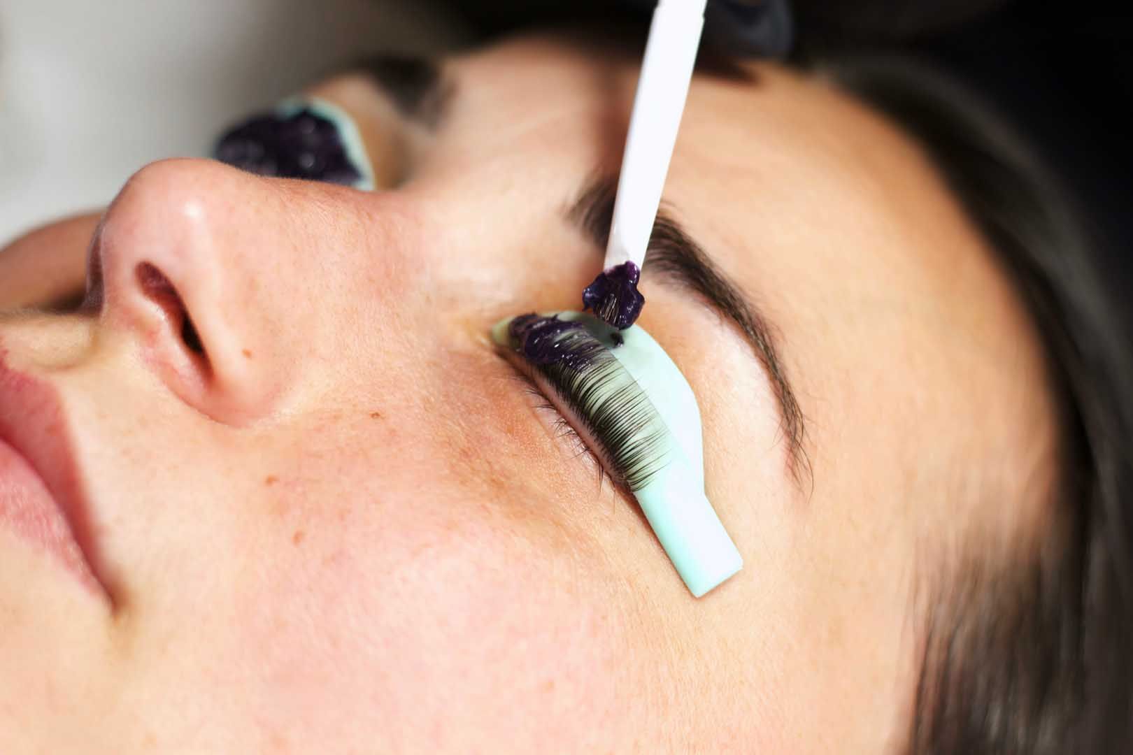 Lash lift procedure: technician applying product to lashes on a client's eye, using a stick applicator.