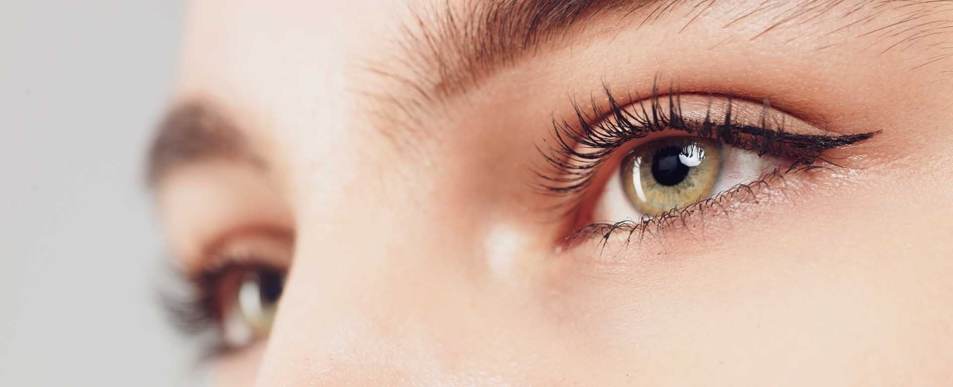 Close-up of an eye with winged eyeliner and mascara. The eye is light green, surrounded by fair skin.