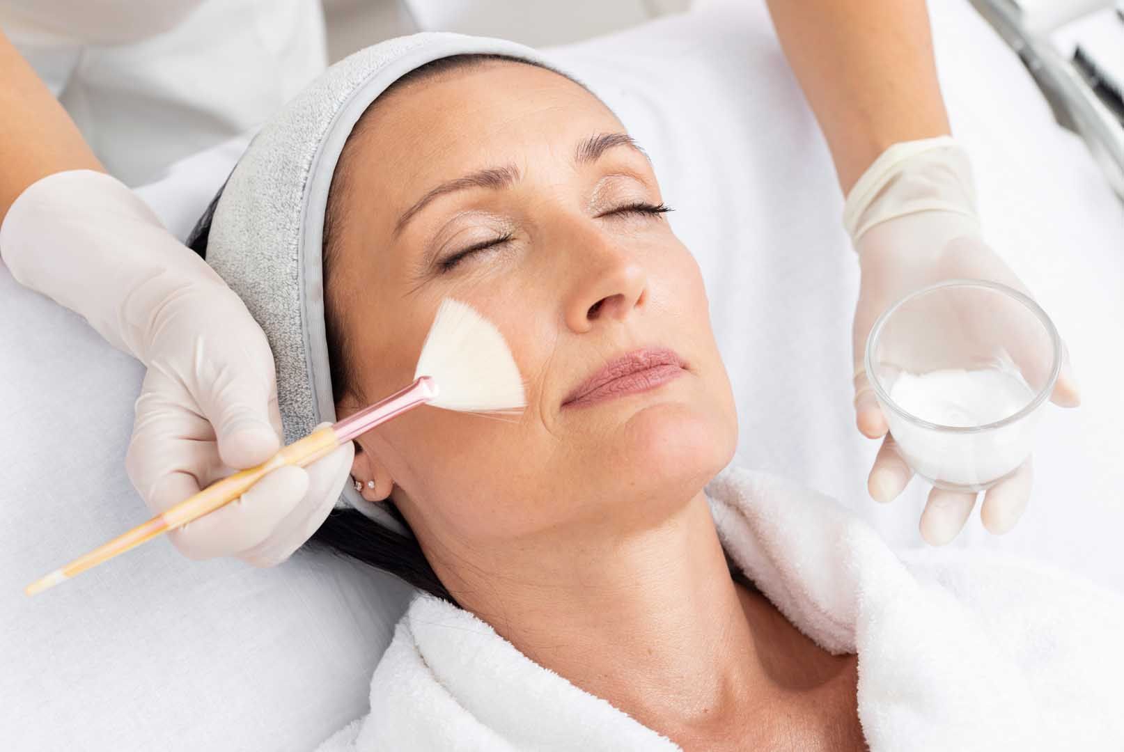 Person receiving facial treatment, application of a mask with a brush, white gloves, close-up.