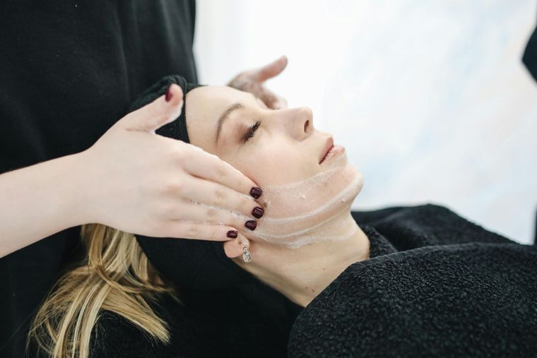 Woman receiving facial treatment; hands applying a mask to her face.