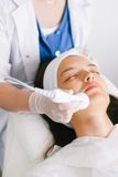 A person receiving a facial treatment. A gloved hand uses a device on the face in a bright setting.