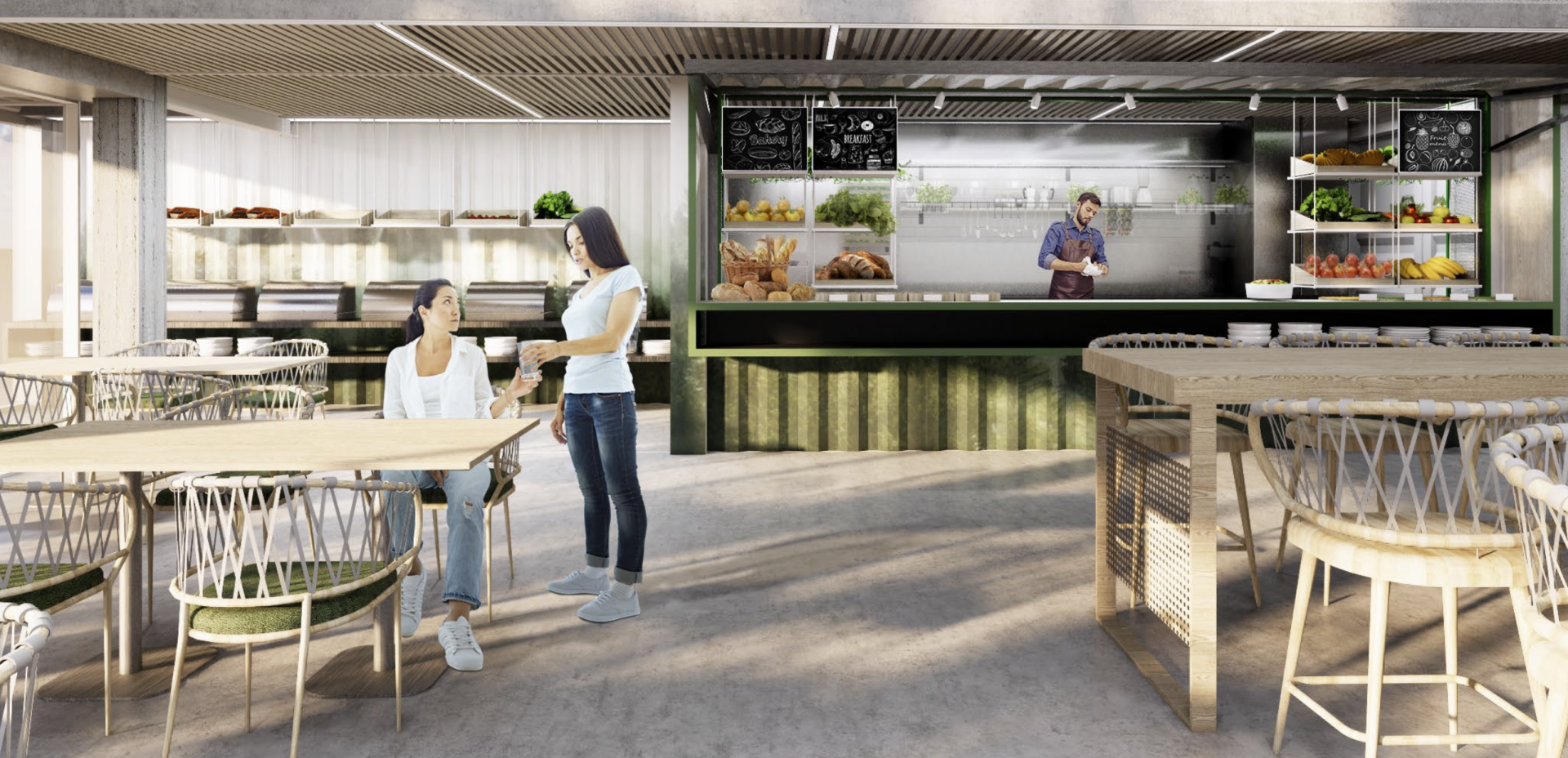 Two women at a table in a cafe, one seated, one standing. A male server prepares food behind the counter.