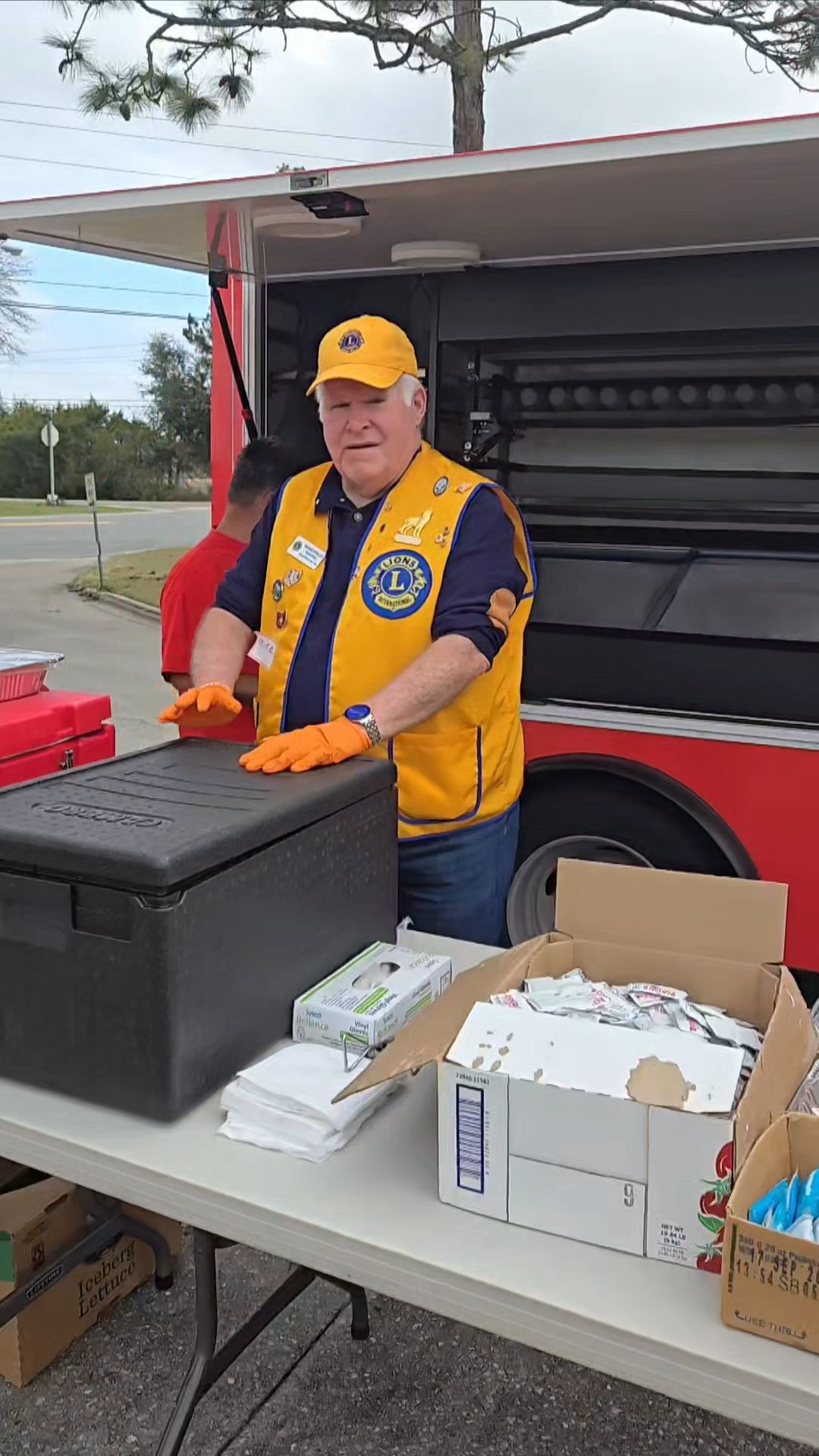 A man in a yellow vest is standing in front of a food truck.