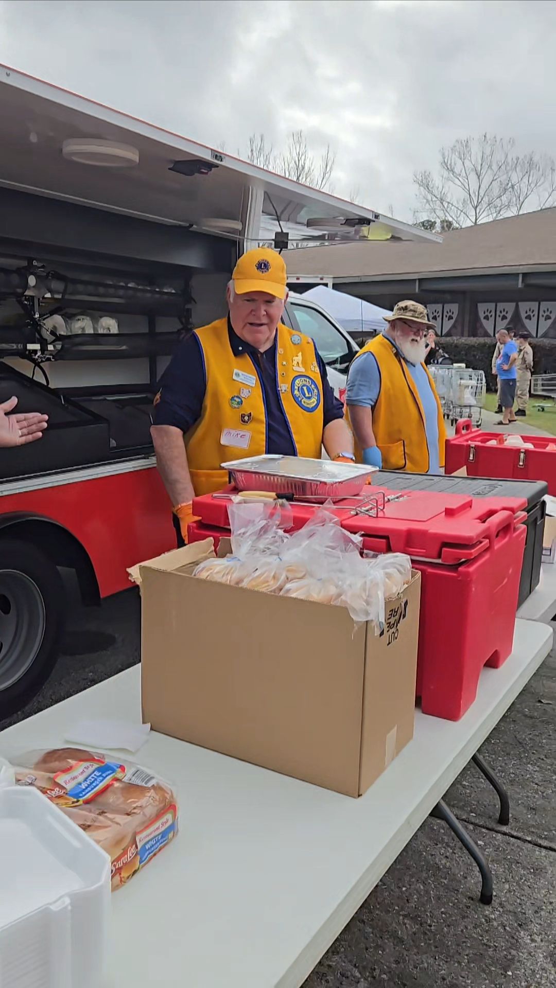 A man in a yellow vest is standing at a table with boxes of food.