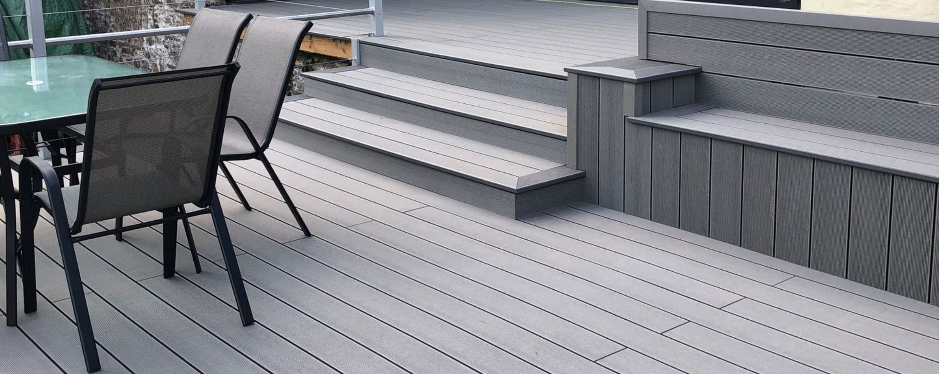 A gray deck with a built-in bench, stairs, and patio furniture.