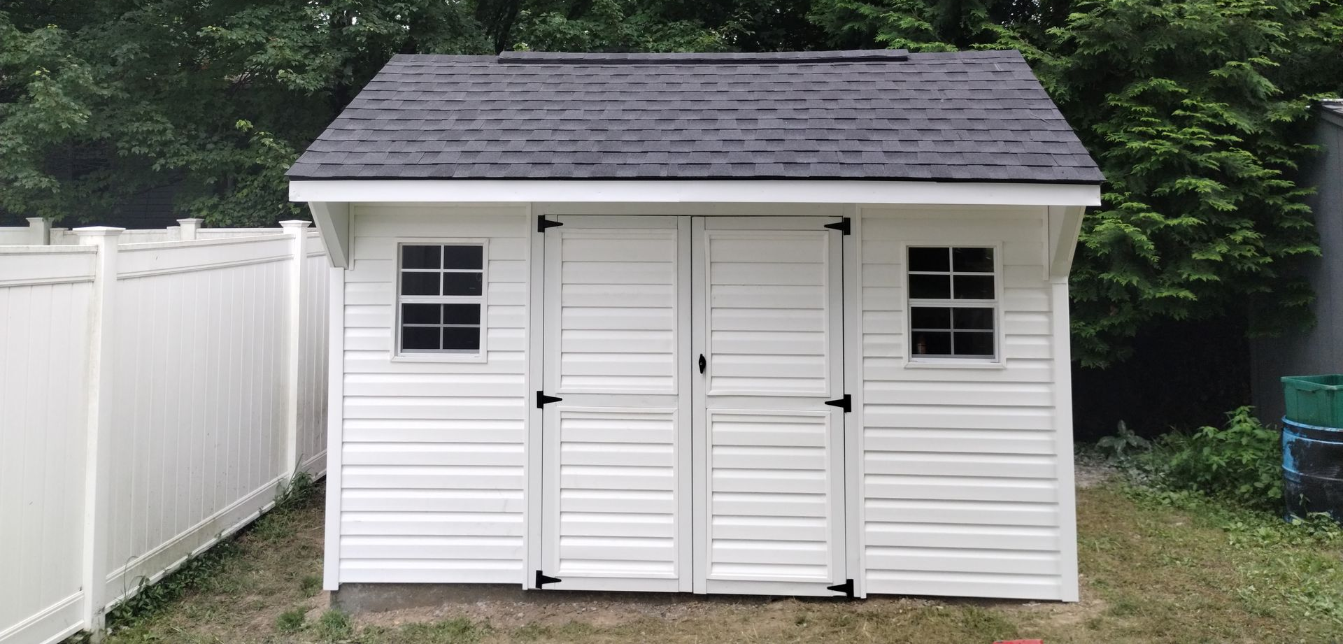 White shed with black roof, two small windows, and double doors.