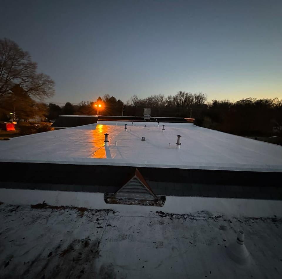 A flat, white commercial roof at dusk, reflecting light.  Several vents and a small, wooden triangle are visible.