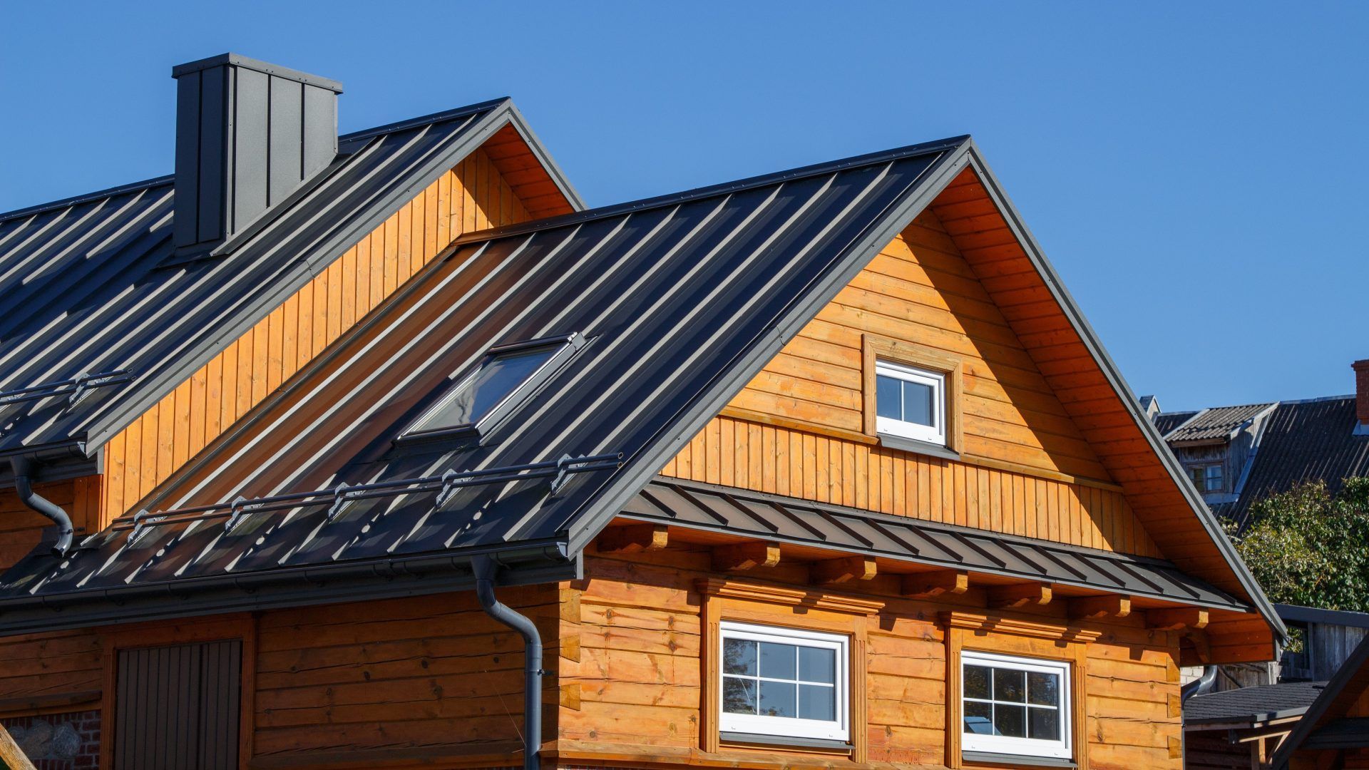 Wooden house with a gray metal roof and small windows against a blue sky.