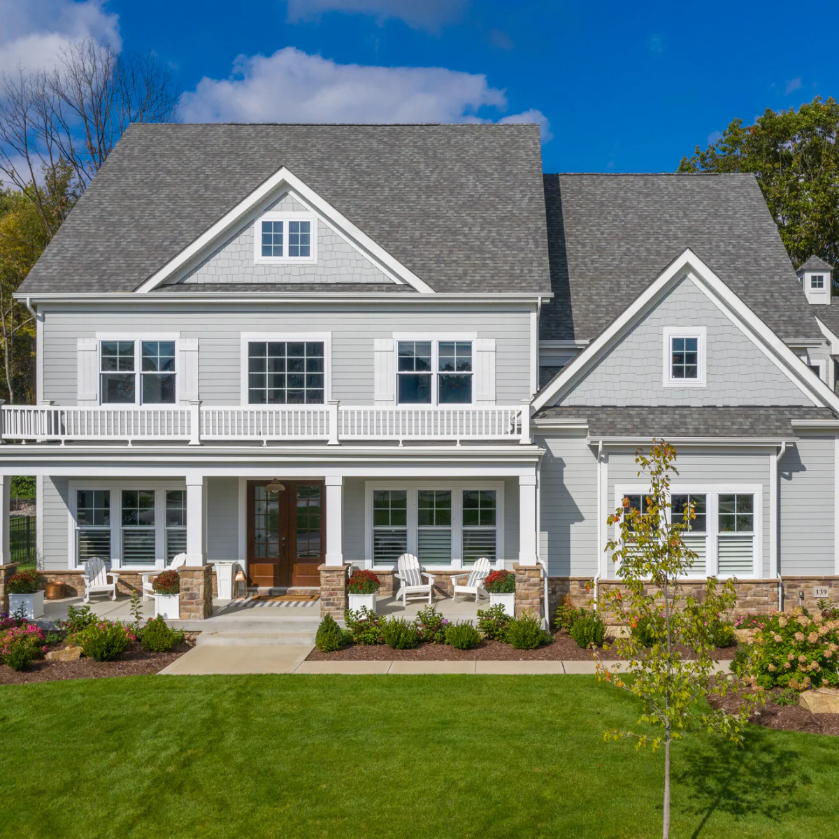 Gray house with white trim, porch, and lawn on a sunny day.
