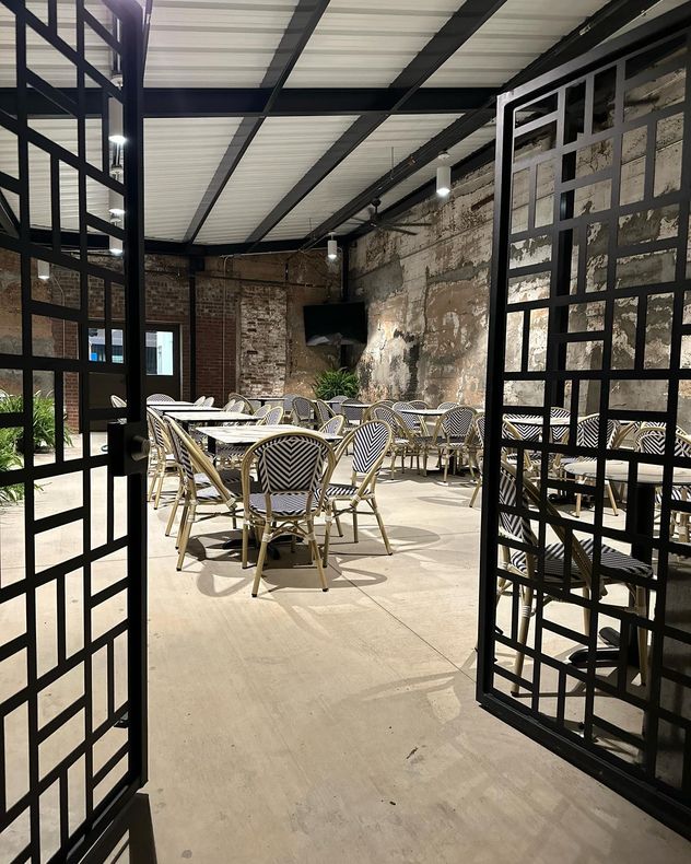 Open doorway to an outdoor restaurant patio with tables and chairs. Brick walls and a metal roof.