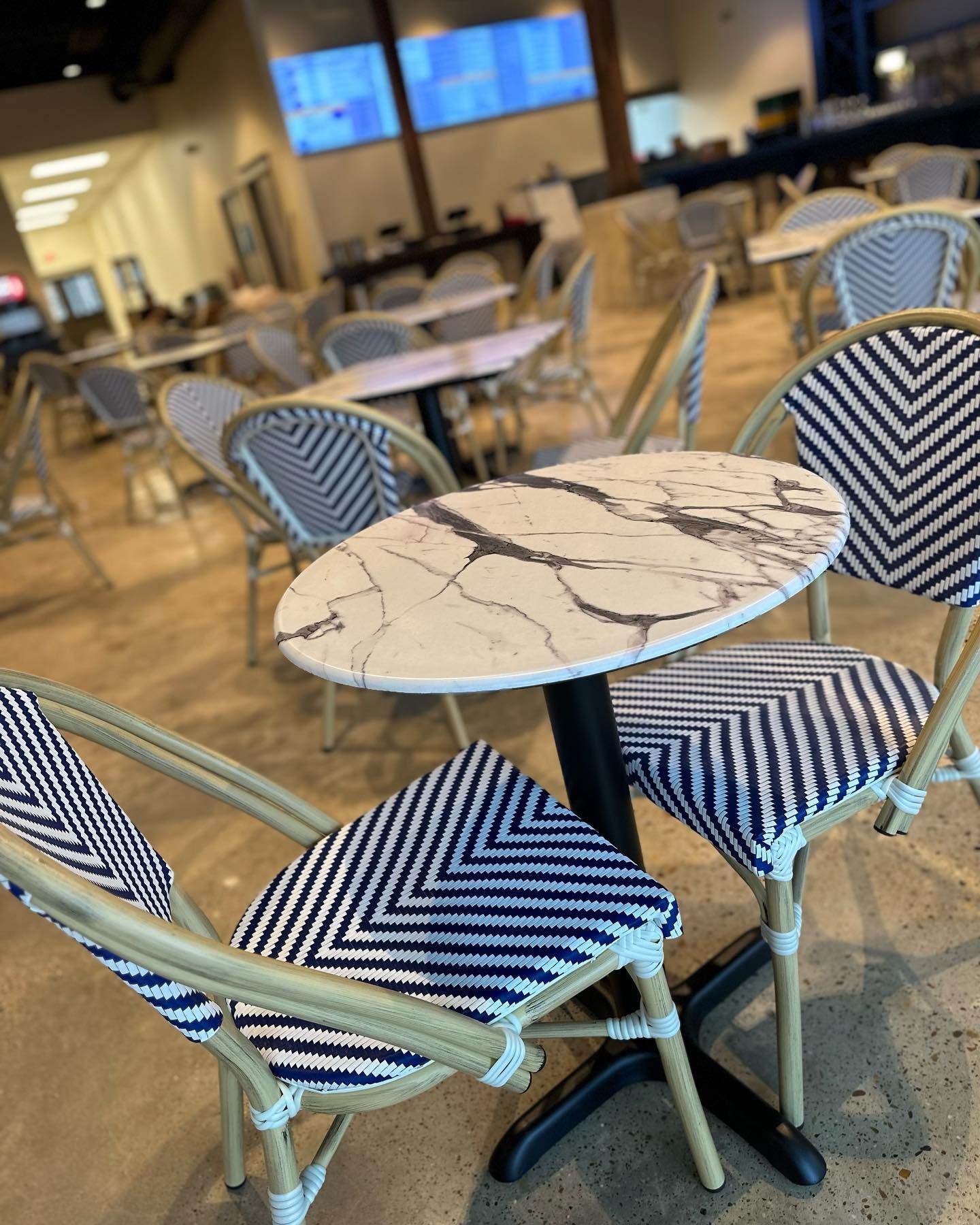 Table with white marble top and two blue-and-white chevron chairs in a cafe setting.