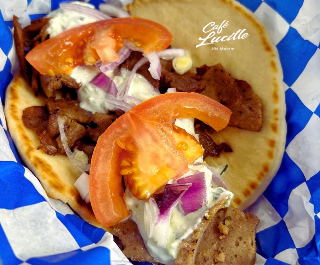 Gyro sandwich with tomato, onion, and tzatziki sauce in a blue and white checkered wrap.