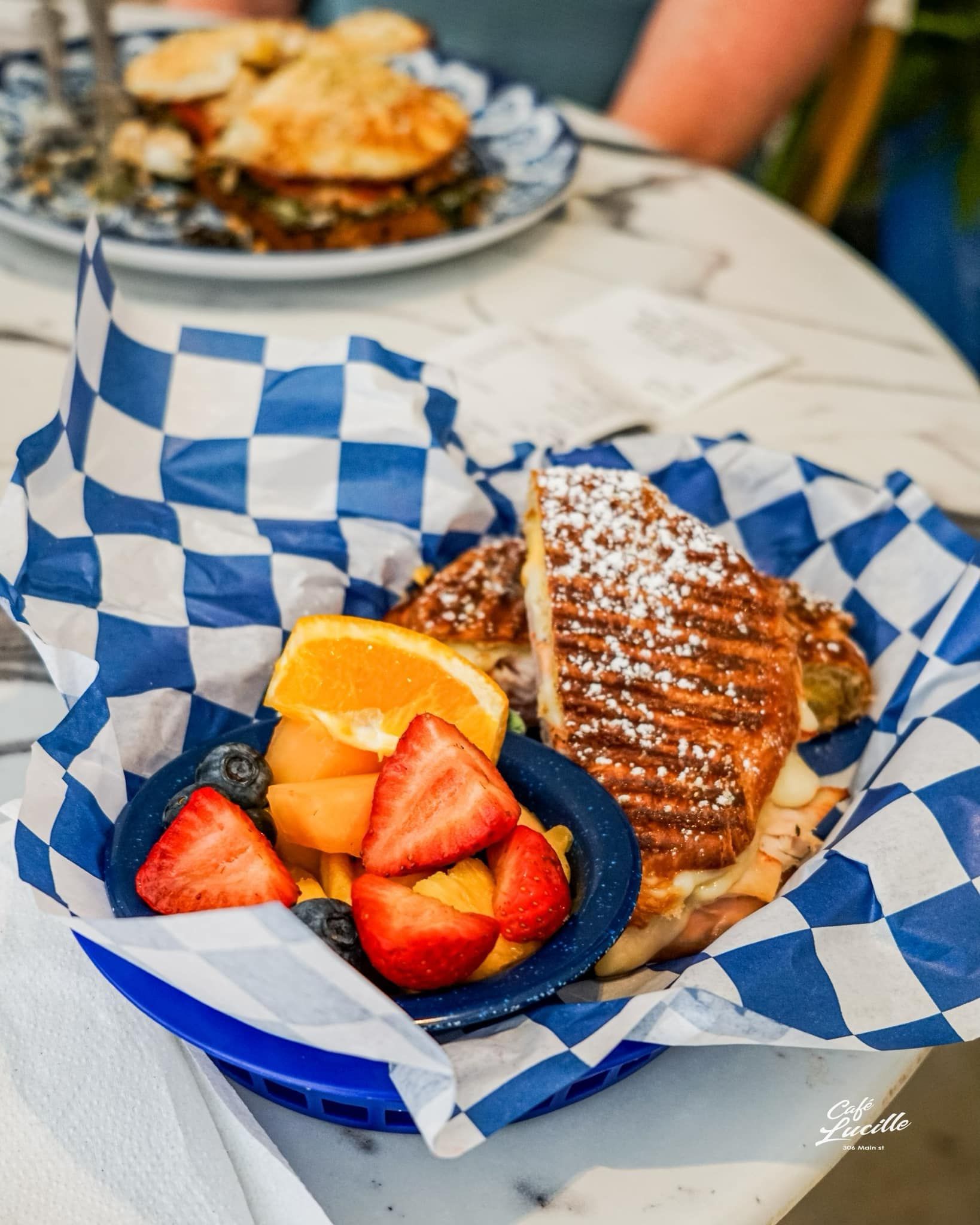 Panini sandwich with fruit in a checkered basket, dusted with powdered sugar.