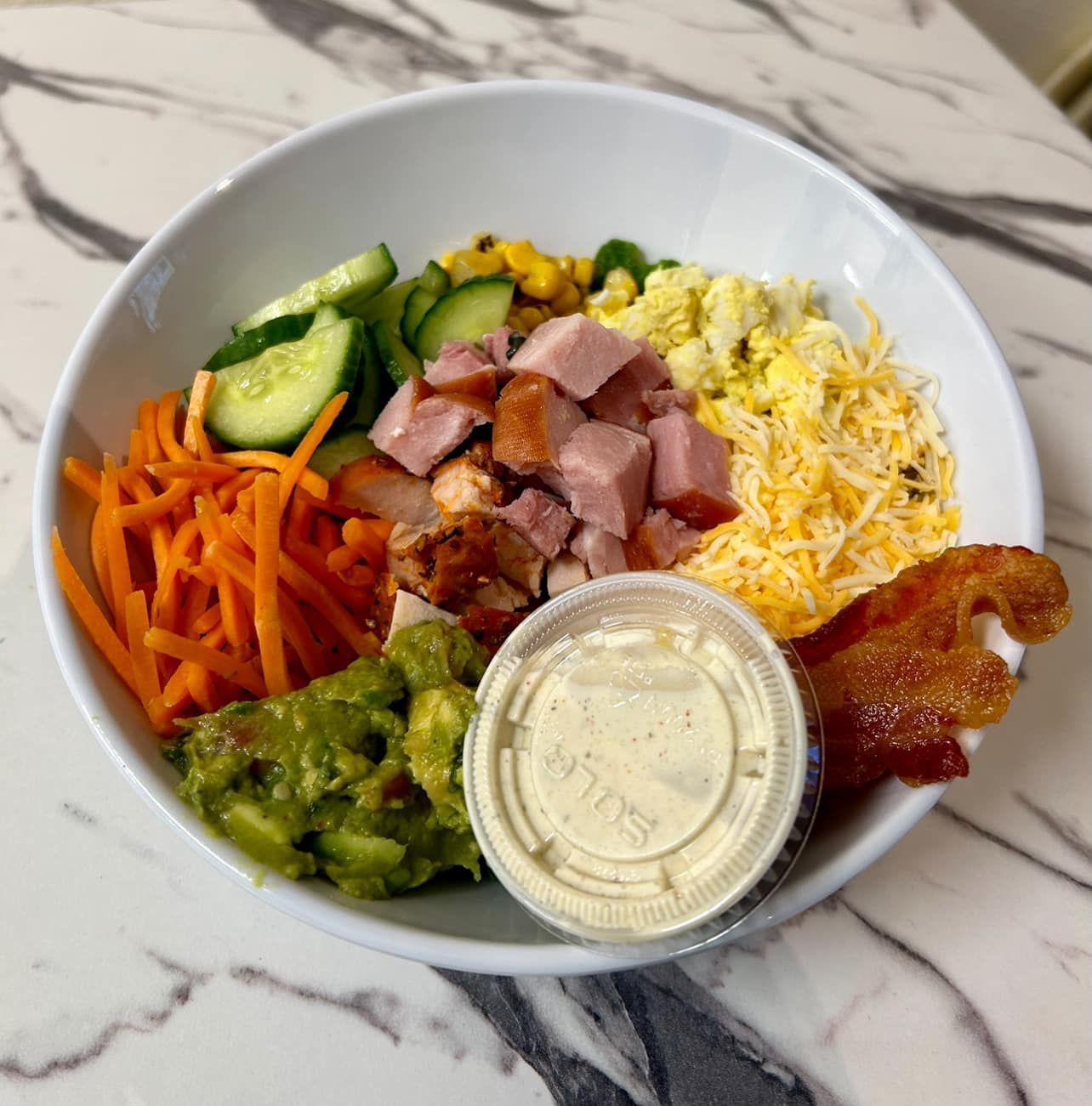 Bowl with ham, cheese, veggies, bacon, and sauce.