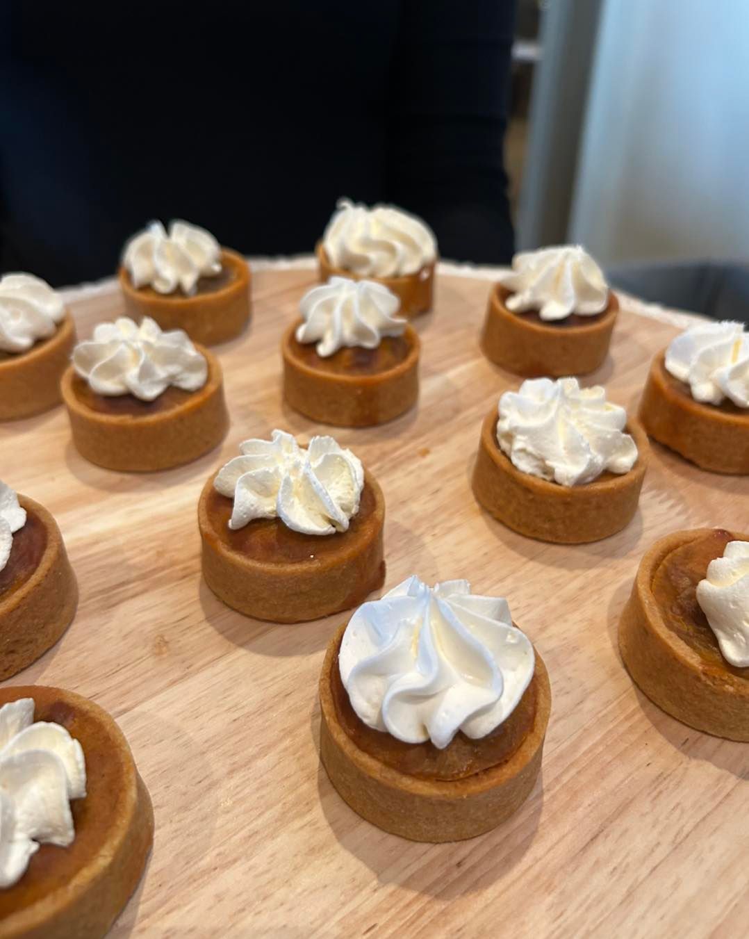 Mini tarts with whipped cream topping on a wooden serving board.