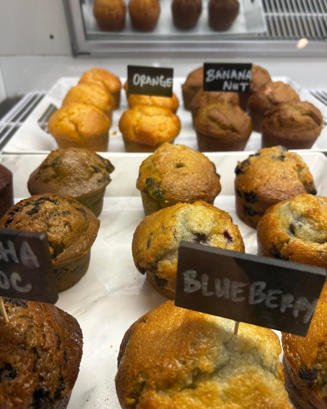 A display of muffins with labels, including blueberry, orange, and banana nut flavors.