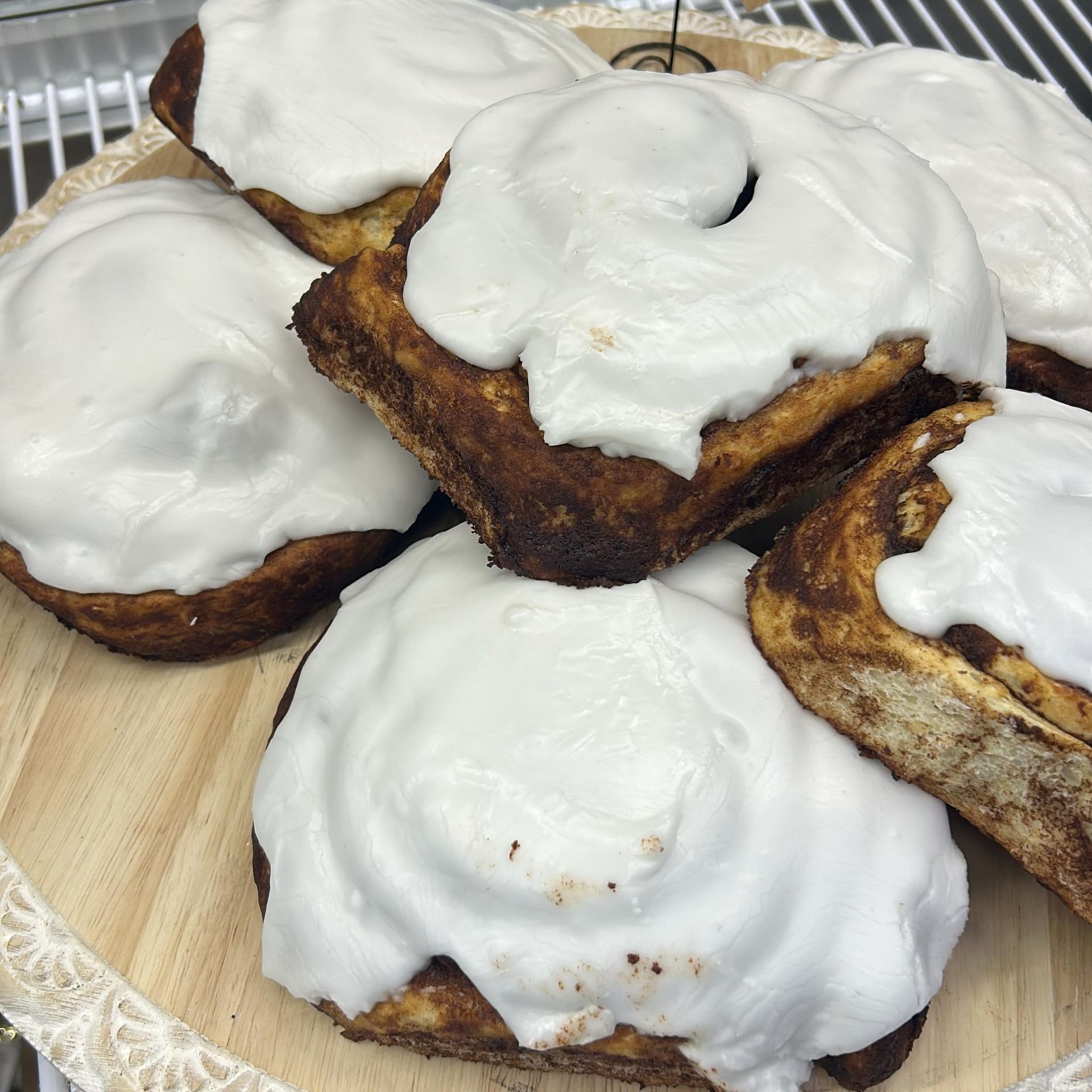 Cinnamon rolls with white icing piled on a wooden platter.
