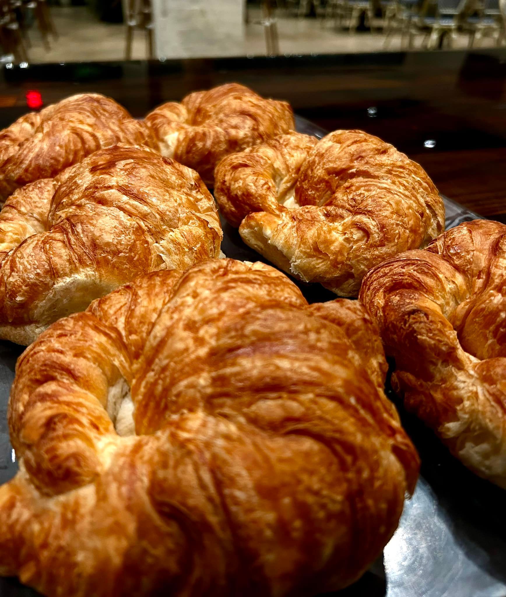 Close-up of golden-brown croissants arranged on a dark surface, some with visible layers.