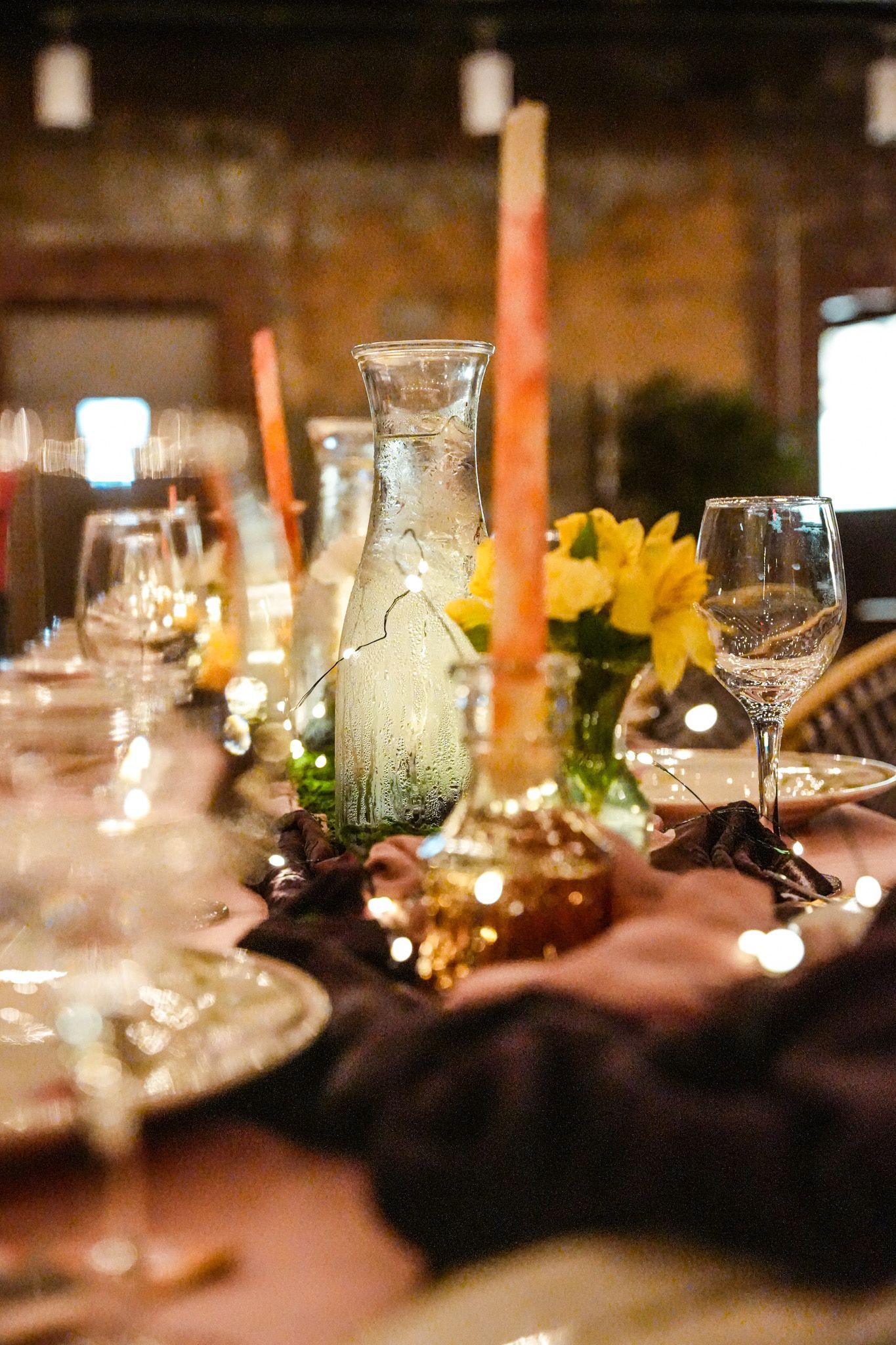 Table setting with candles, glasses, flowers, and string lights.