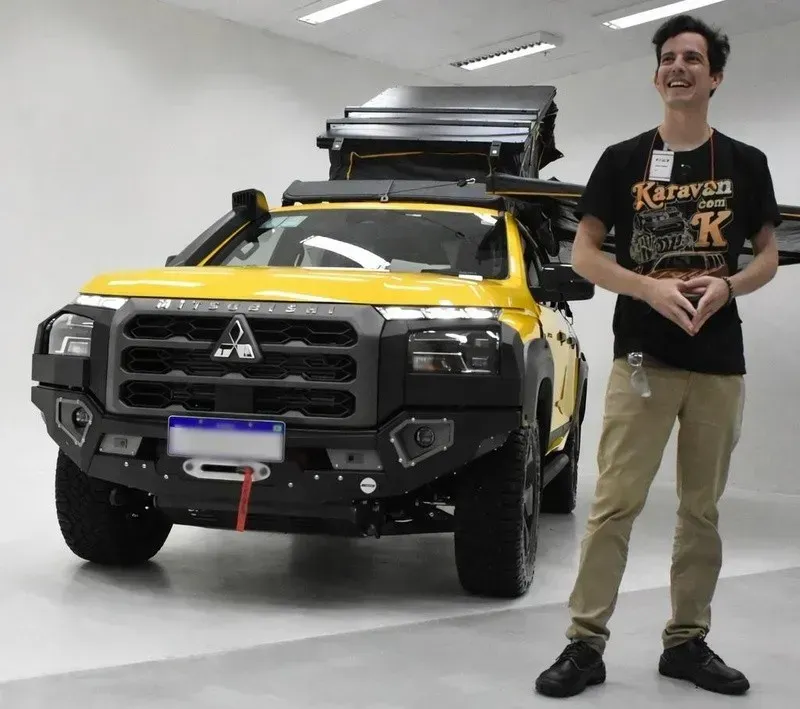 SUV Mitsubishi amarela e preta com bagageiro de teto, estacionada em local fechado ao lado de um homem em pé.