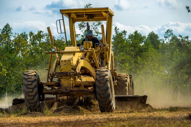 A man is driving a yellow tractor through a dirt field.
