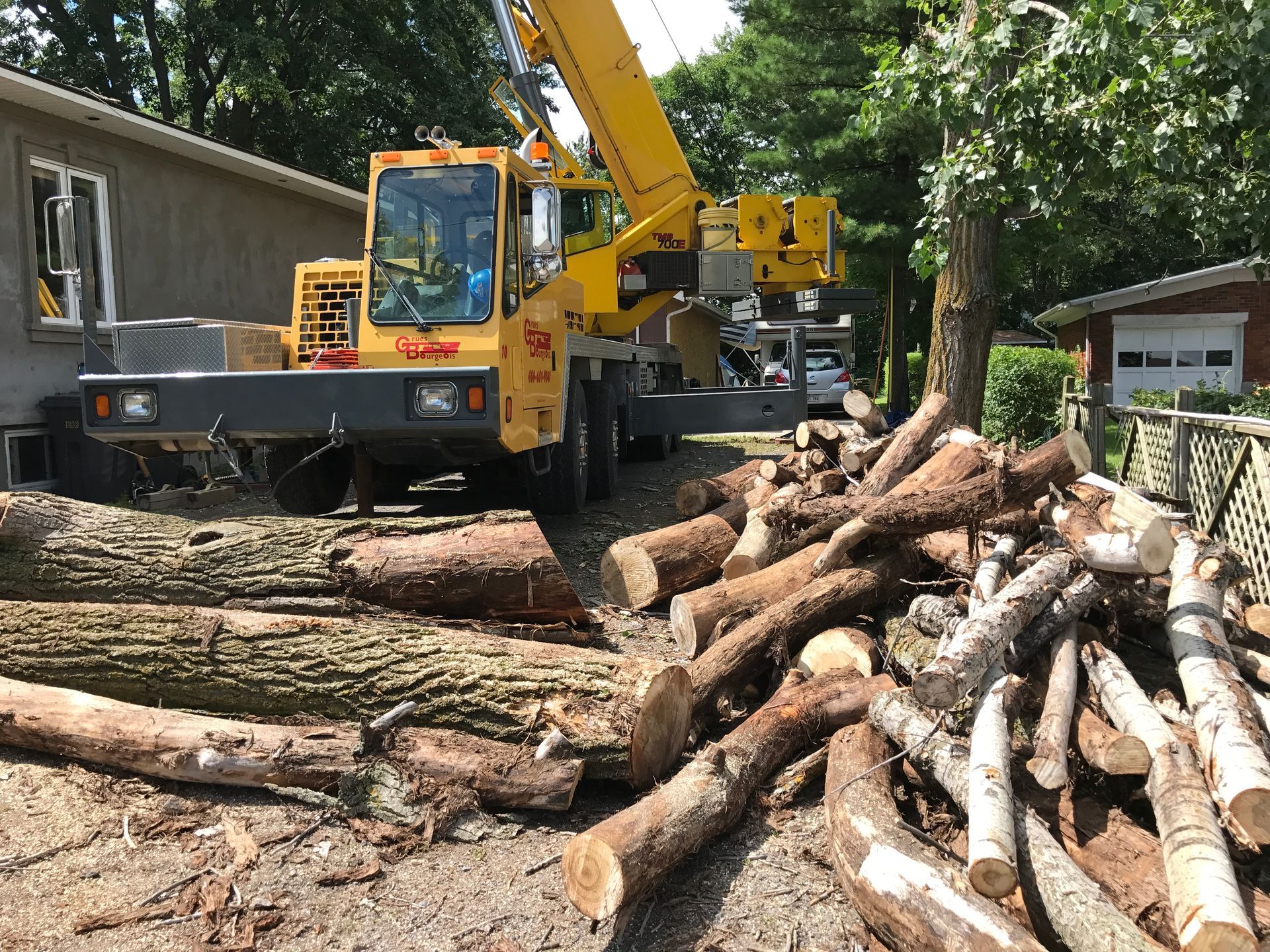 Une grue abat un arbre devant une maison.