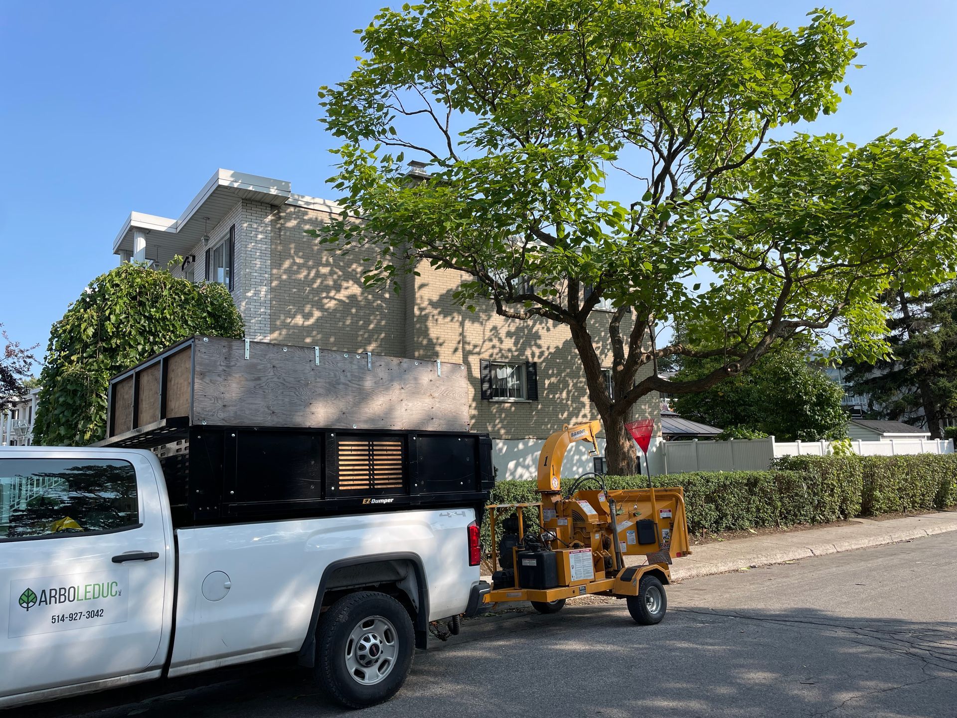 Un camion blanc avec un broyeur d'arbres attaché est garé devant une maison.