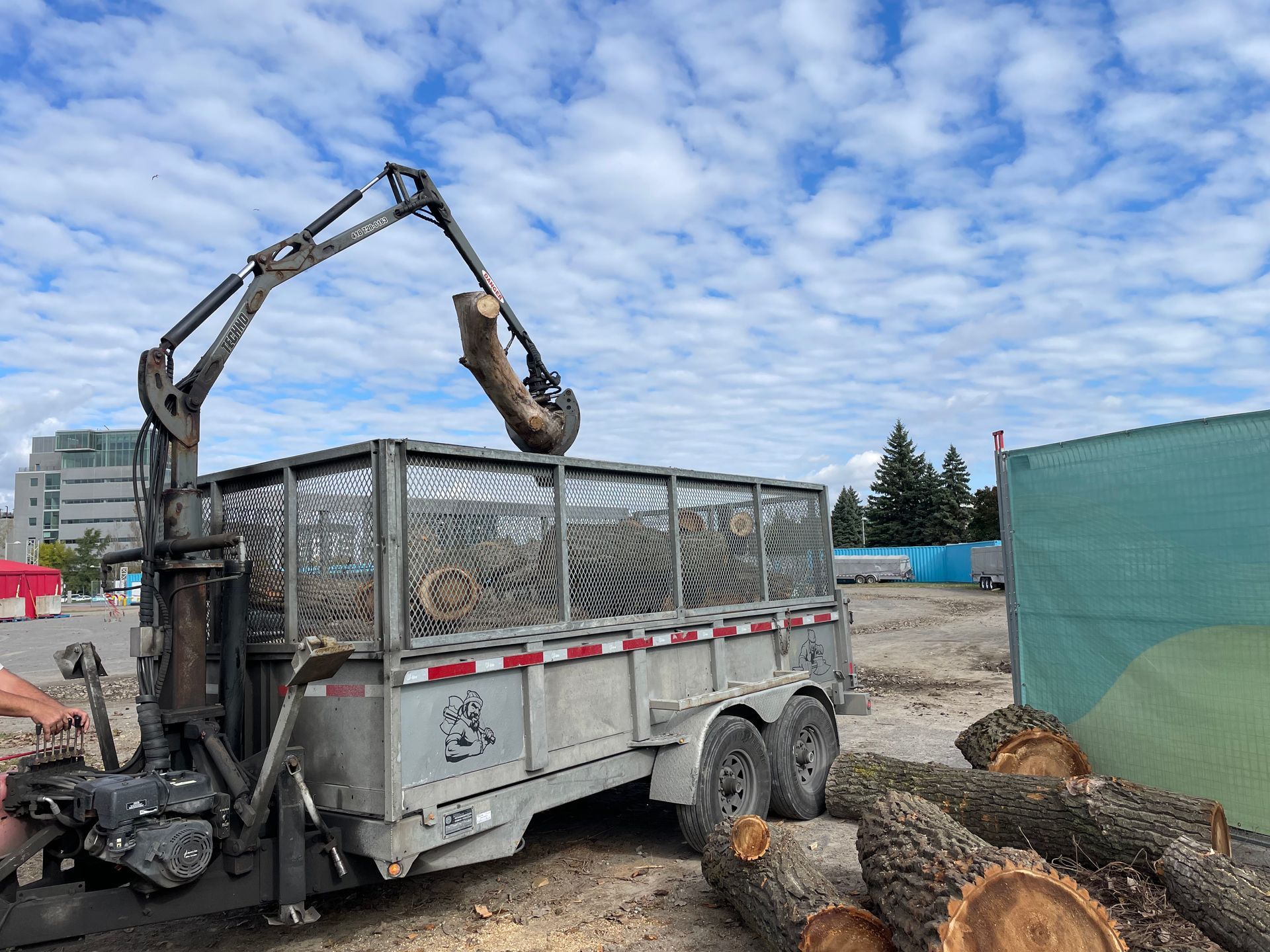 Une remorque avec une grue attachée est en train d'être chargée de grumes.