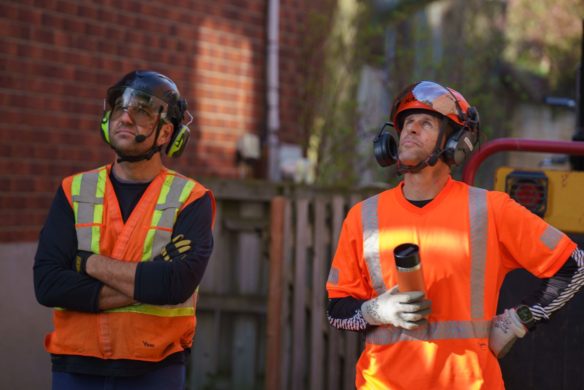 Deux ouvriers du bâtiment portant des gilets de sécurité et des casques se tiennent l'un à côté de l'autre.