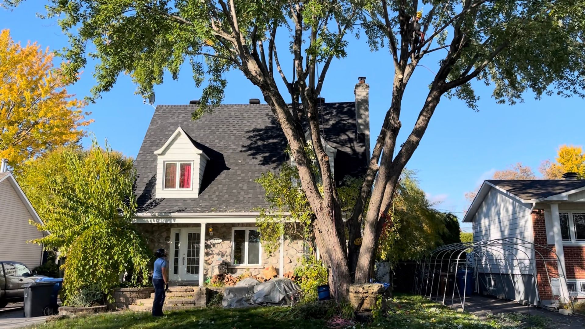 Un homme se tient devant une maison avec un arbre devant.