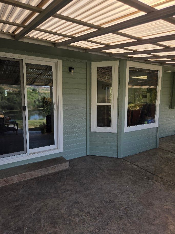 A light green house with white-framed windows and a sliding door, under a covered patio.